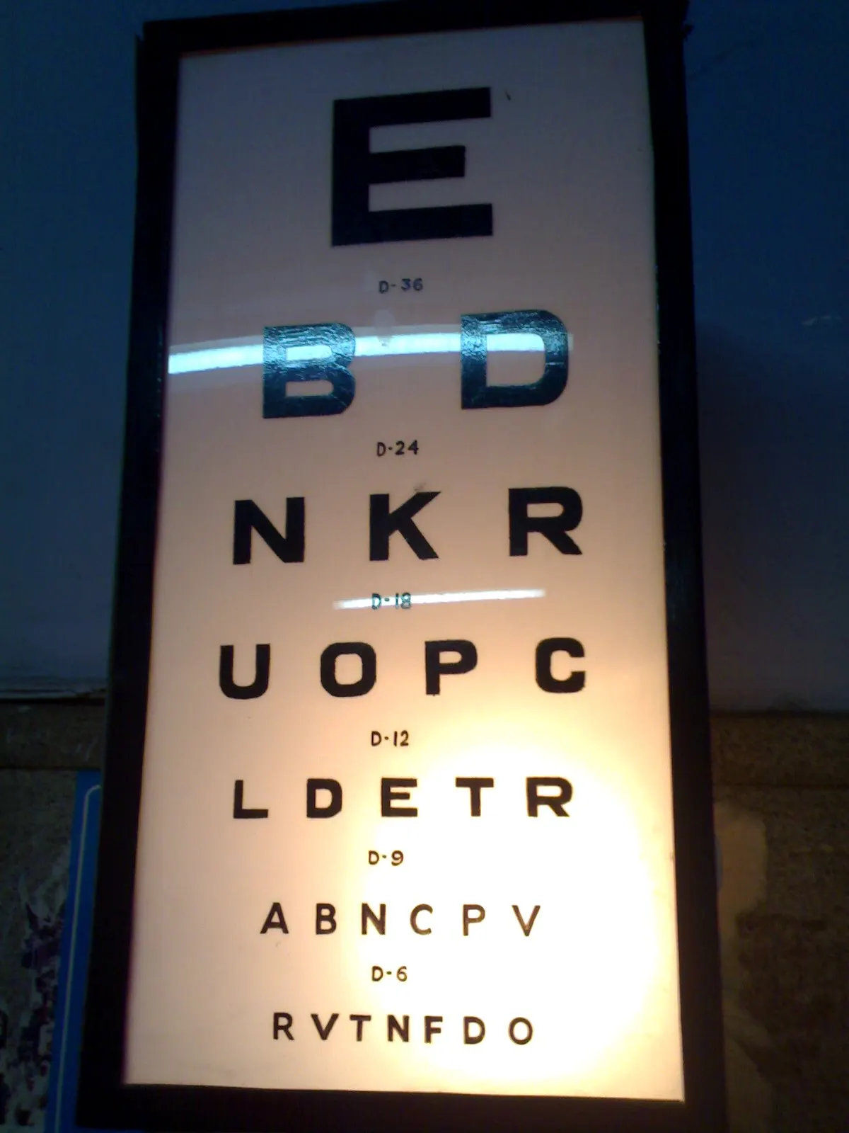 A backlit Snellen eye chart with rows of black letters, largest at the top
